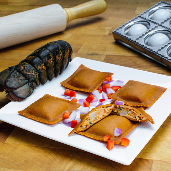 Plated lobster ravioli garnished with diced peppers next to a rolling pin, pasta mold, and cooked lobster tail.